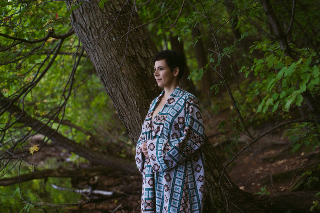 josie looks at lake wearing a cloak and very serene