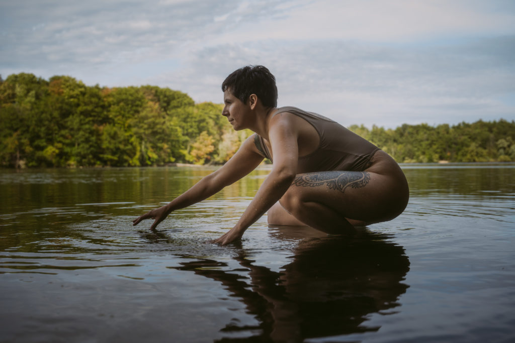josie-crouches-in-the-lake-as-hands-skim-water